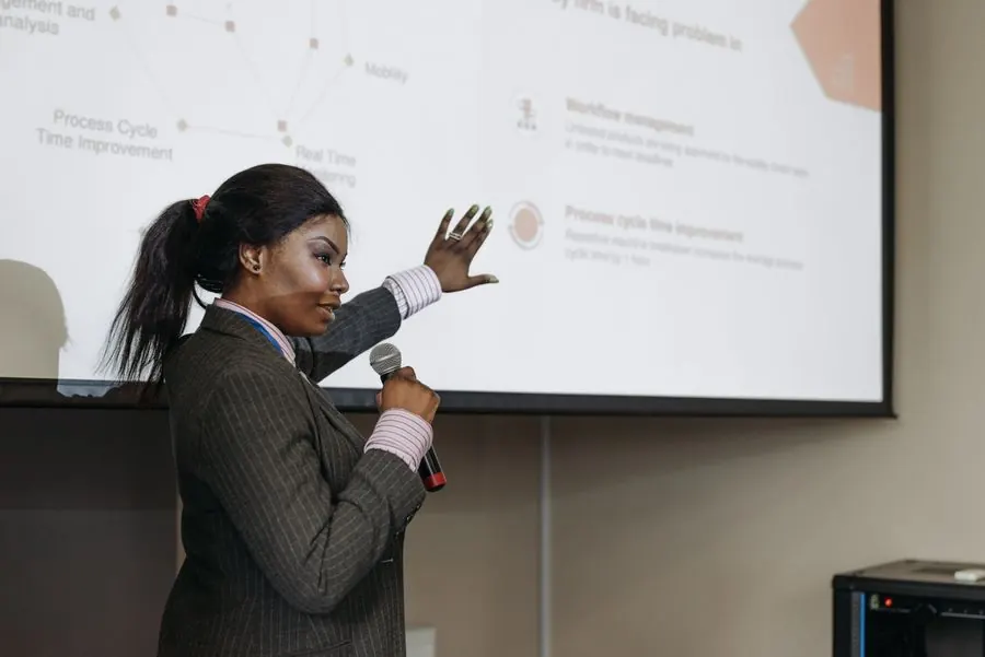 A woman with a microphone presenting slides at a conference